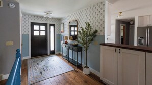 Un couloir avec un plancher en bois, une rambarde bleue, une plante en pot, un miroir et un réfrigérateur.