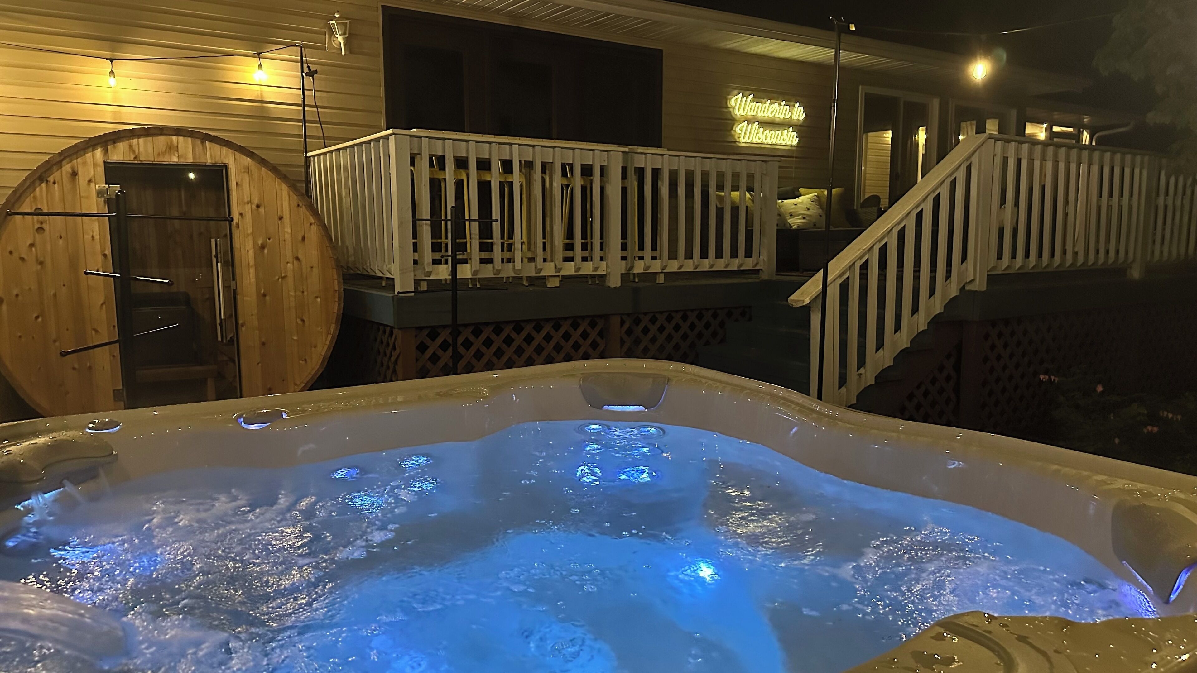 A hot tub with a wooden deck and a staircase leading to a balcony.