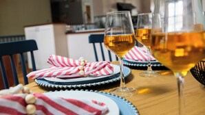 Une table à manger avec trois verres à vin remplis d’une boisson dorée, des serviettes à rayures et des assiettes bleues ornées de perles dorées.