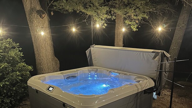 Un bain à remous avec un marchepied, entouré d’arbres et illuminé de guirlandes lumineuses.