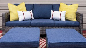Un canapé en osier agrémenté de coussins bleus et d’oreillers à motifs jaunes, posé sur un tapis rayé rouge et blanc.