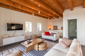 Een moderne woonkamer met een flatscreen televisie, een witte bank, een houten salontafel en een gestreept vloerkleed.