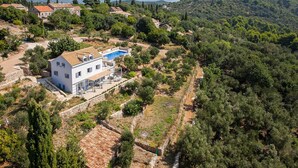 Un ampio edificio bianco con una piscina, circondato da alberi e colline.