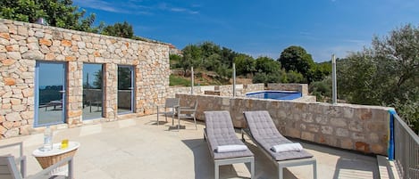 A stone building with a pool, lounge chairs, and a table with a bottle and glasses.