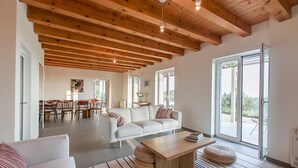 Un'ampia zona giorno con soffitto alto, un divano bianco, un tavolino da caffè e, sullo sfondo, una zona pranzo.