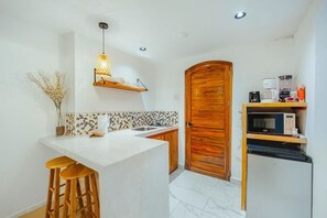 Eine kleine Küche mit einer weißen Arbeitsplatte, Holzstühlen, einer Holztür und einer Mikrowelle.