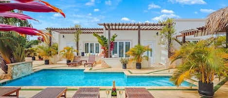 Ein Poolbereich mit Liegestühlen, einem Tisch mit Flasche und Gläsern, und einem Gebäude mit einer Pergola.
