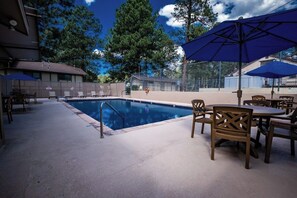 A swimming pool with lounge chairs and umbrellas, surrounded by trees and a building. - Innsbrook Vacation Condo 30 (Ruidoso)