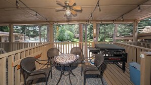 Een terras buiten met een ronde tafel, vier stoelen, een plafondventilator en een barbecue.