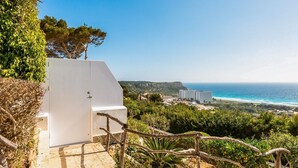 A white building with a staircase leading to a balcony overlooking a coastal landscape with a clear view of the sea and distant buildings. - Apartment Las Vistas (Alayor)