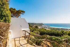 Ein weißes Gebäude mit einer Treppe, die zu einem Balkon führt, der auf eine Küstenlandschaft mit freiem Blick auf das Meer und entfernte Gebäude blickt.