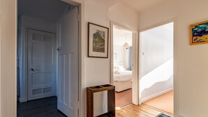Un couloir avec un plancher en bois, un tableau encadré au mur et une porte donnant sur une chambre à coucher.
