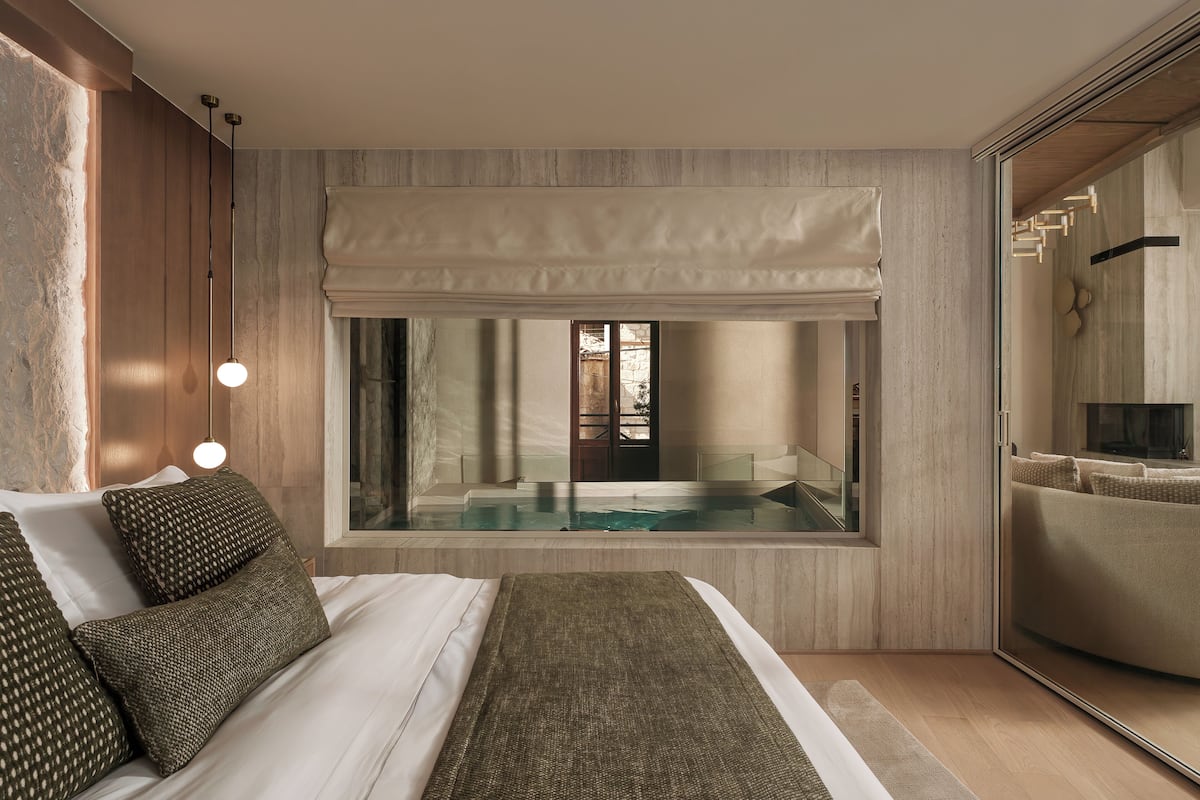 A modern bedroom with a large bed, a view of a pool, and a sliding glass door leading to a bathroom.