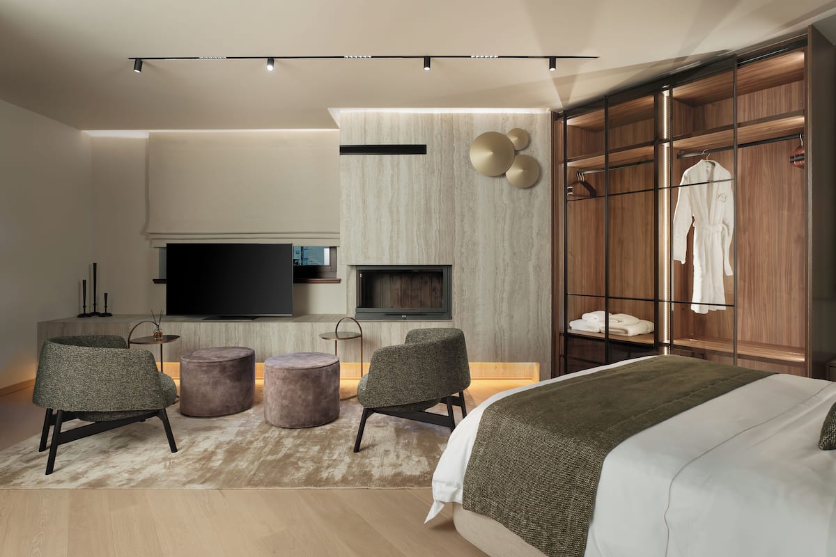 A modern bedroom with a large bed, a TV, a wardrobe, and a seating area with ottomans.