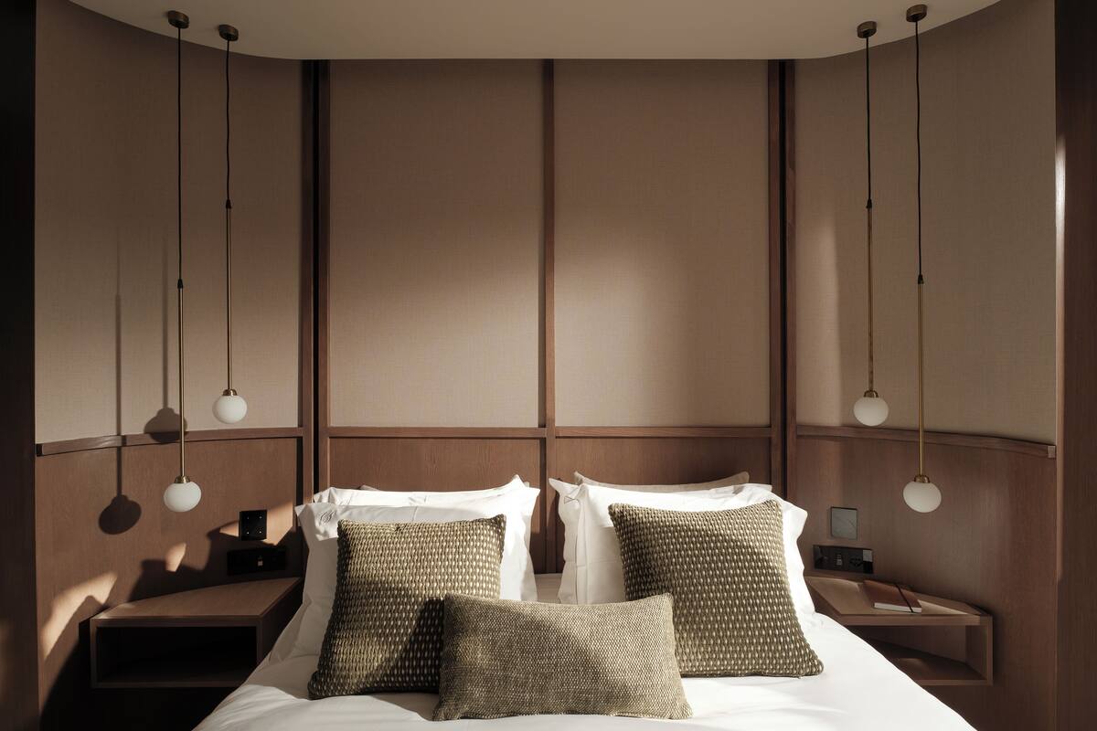 A modern hotel room with a large bed, two bedside tables, and hanging pendant lights.