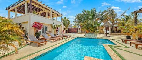 A swimming pool with lounge chairs and a pergola, surrounded by tropical plants.