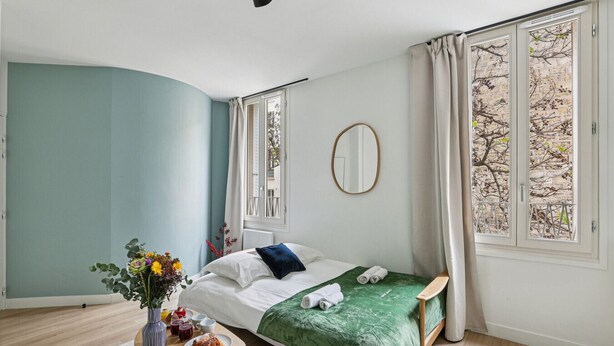 Un dormitorio moderno con una cama, una mesita de noche con un florero y vistas a árboles por la ventana.