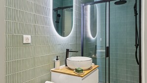 Un baño moderno con ducha envuelta en vidrio, un espejo redondo y un lavamanos blanco con encimera de madera.