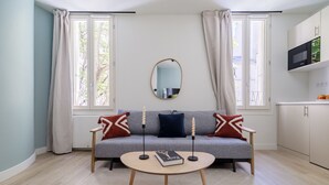 Una sala de estar moderna con un sofá gris, dos mesas auxiliares, una mesa de centro redonda y un pequeño espejo en la pared.