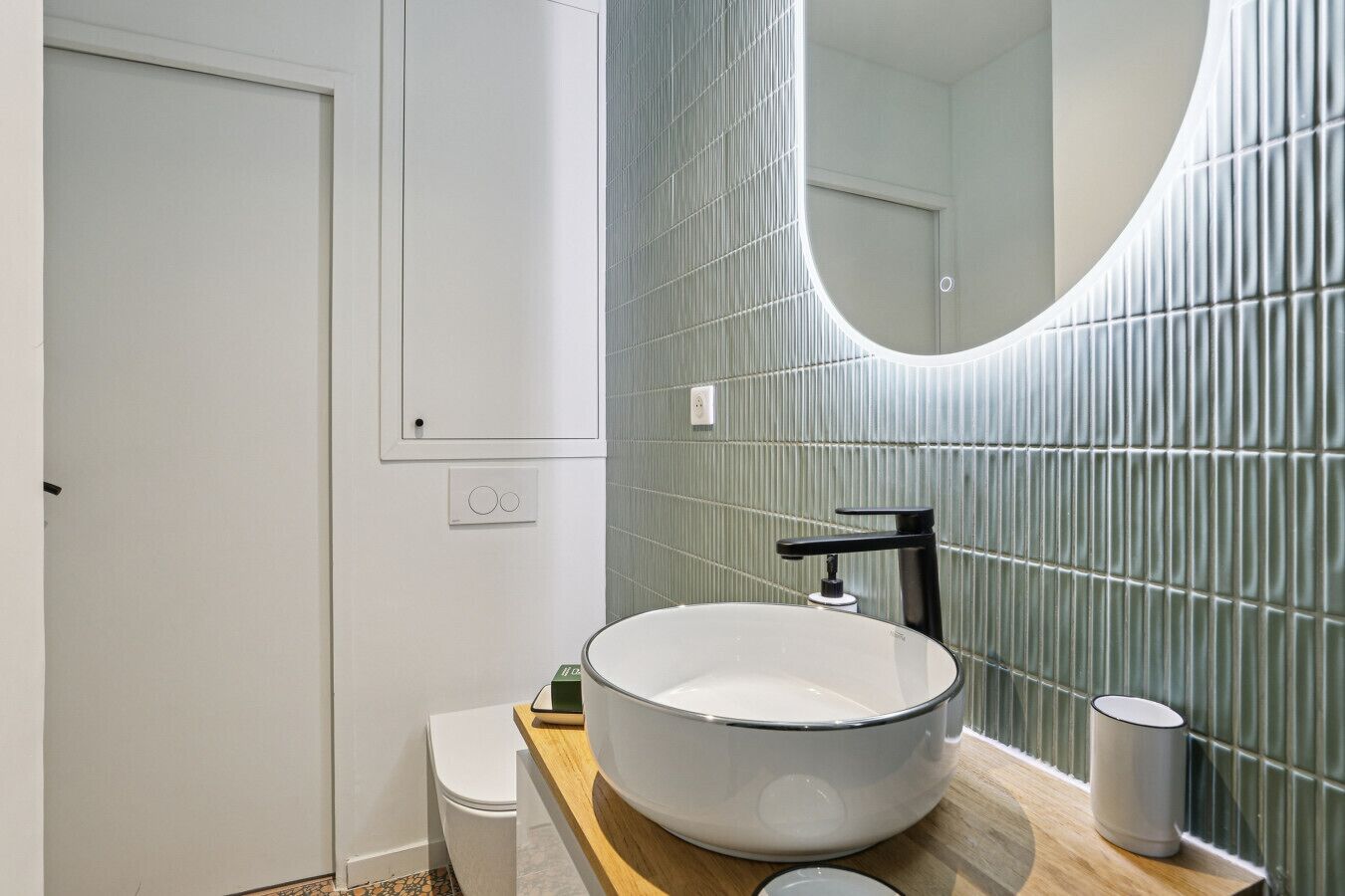 A modern bathroom with a large oval sink, a toilet, and a mirror with a curved frame.