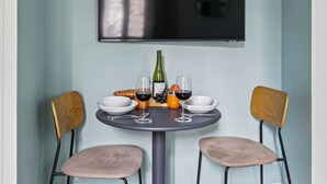 Un comedor con una mesa redonda, dos sillas, una botella de vino, copas y un croissant.