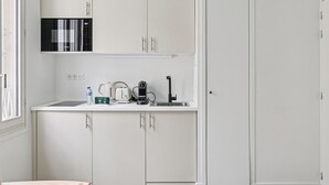 Una kitchenette compacta con armarios blancos, un microondas, un hervidor, un tostador y un lavamanos.