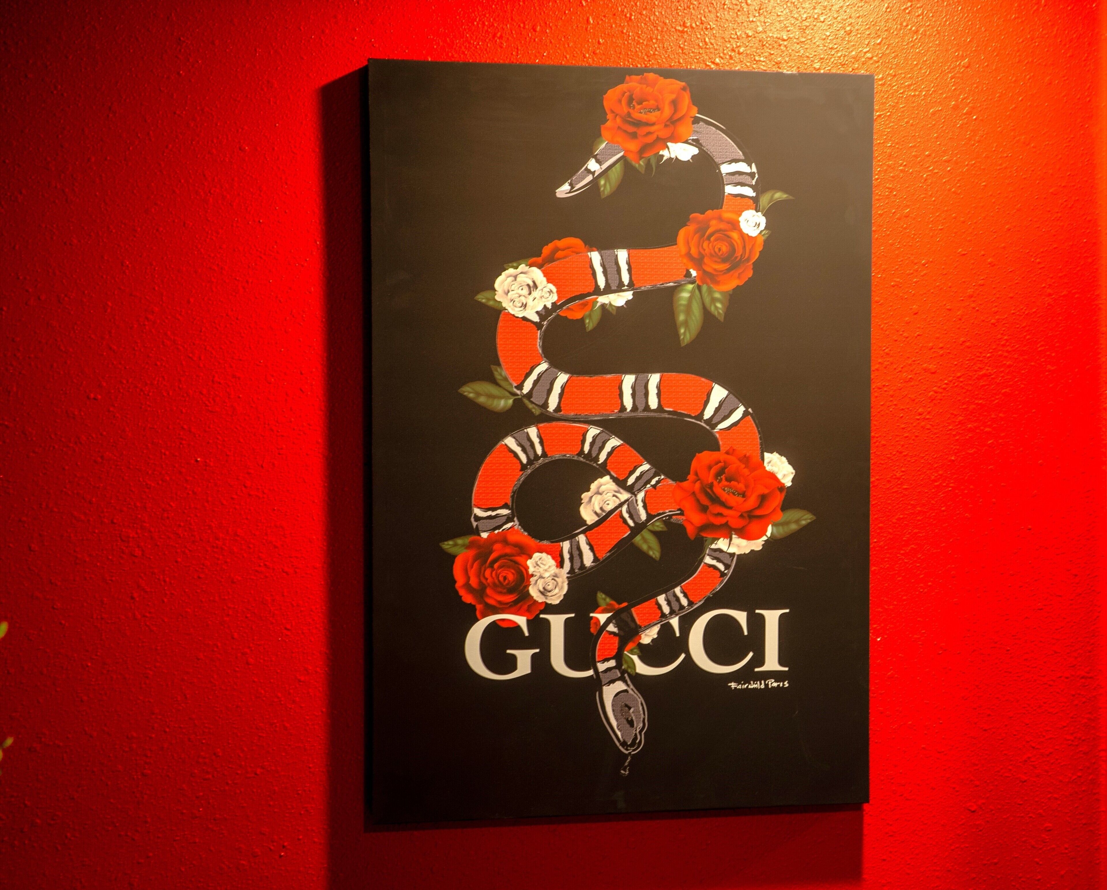 Une œuvre d’art Gucci encadrée, accrochée à un mur rouge.