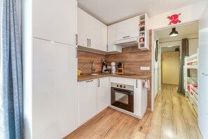 Een kleine keuken met witte kasten, een houten aanrechtblad, een inbouwoven en een klein spoelbakje.