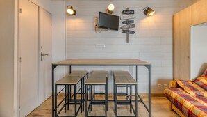 Pieni huone, jossa on sänky, neljän tuolin ruokapöytä, seinälle asennettu televisio ja opastekylttejä.
