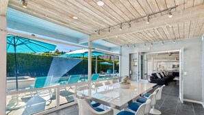 A modern kitchen with stainless steel appliances, a dining area with a glass table and chairs, and a view of a pool area. - Azure Palms at Deepwell – Luxury Pool Retreat (Palm Springs)