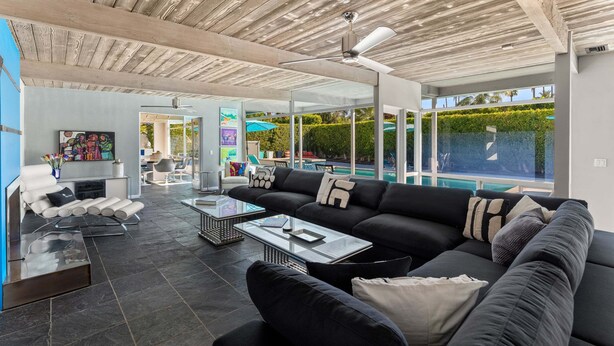 A modern living room with a black sofa, a glass coffee table, and a ceiling fan. - Azure Palms at Deepwell – Luxury Pool Retreat (Palm Springs)