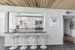 Una cocina moderna con una isla central, taburetes de bar, armarios blancos y un microondas.