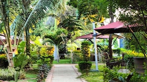 A pathway flanked by lush greenery and a red-roofed structure. - The Heritage Resort (Wajir)