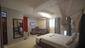 A hotel room with a large bed, a sofa, a TV, and a mirror. - The Heritage Resort (Wajir)