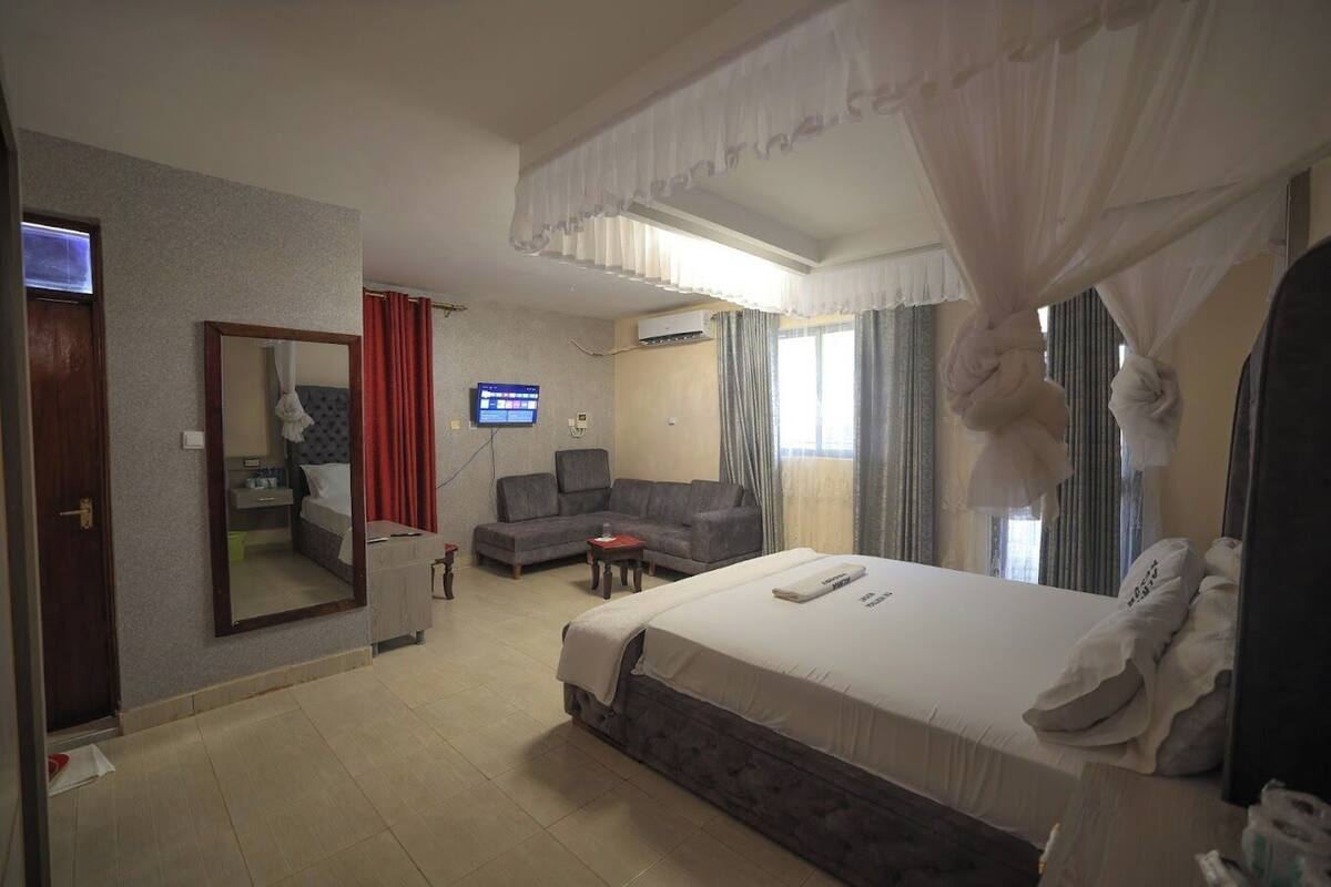 A hotel room with a large bed, a sofa, a TV, and a mirror.