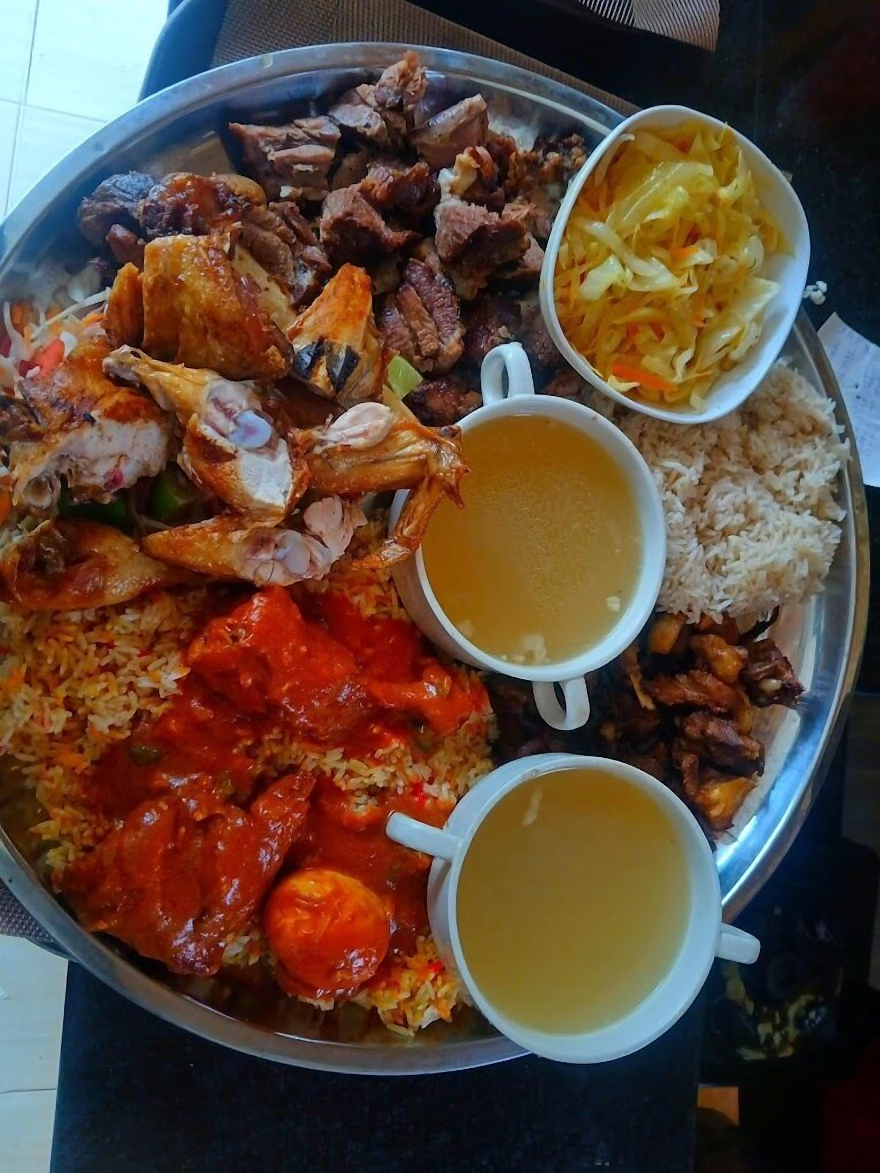 Un plato de metal con arroz, pollo, carne y dos tazones de sopa.