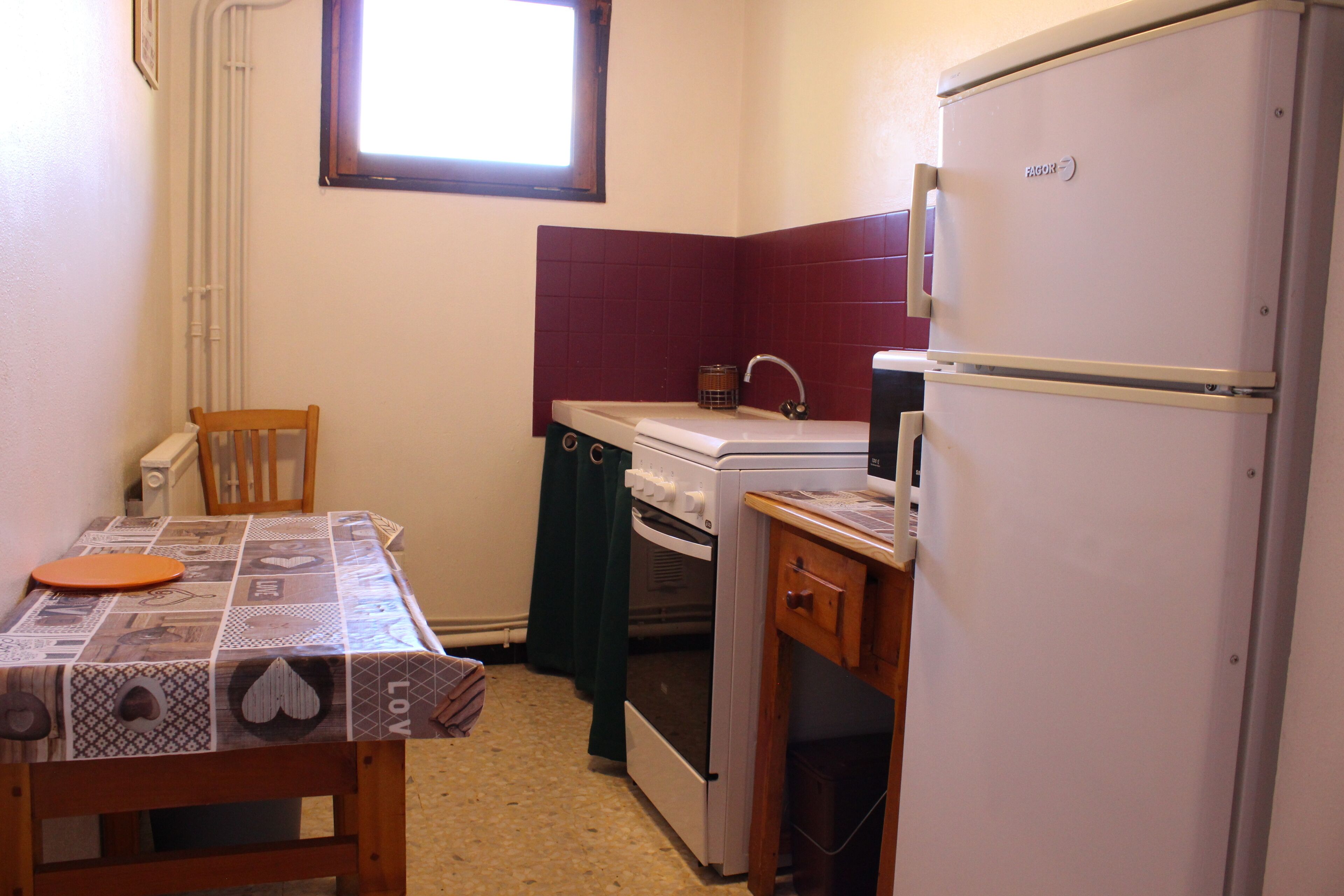 Een kleine keuken met een tafel, stoel, oven en koelkast.