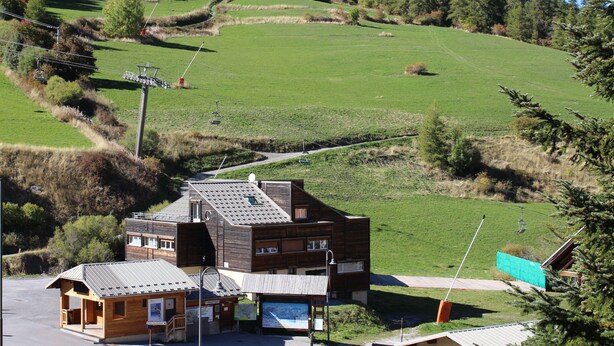 Un edificio moderno con tetto spiovente, una piccola struttura adiacente e una vista aperta su un pendio verde.