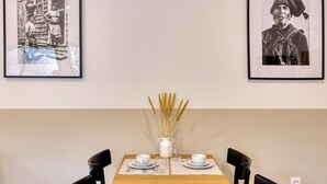 Un comedor con una mesa de madera dispuesta para dos personas, fotografías en blanco y negro en la pared, y un jarrón con cañas sobre la mesa.