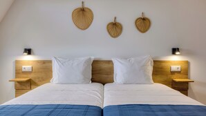 Una cama doble con cabecera de madera, dos mesitas de noche con lámparas, y tres elementos decorativos colgados en la pared.