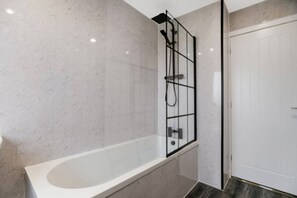 Un baño moderno con una bañera independiente, cabina de ducha con mampara de vidrio y una puerta blanca.