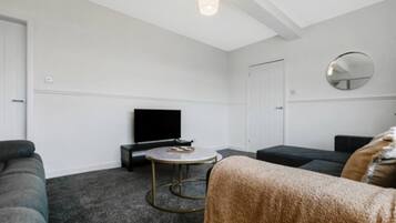 A living room with a flat-screen TV, a round coffee table, and a sofa.