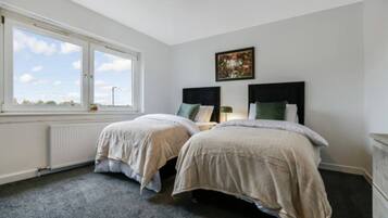A bedroom with two beds, a radiator, a window with a view, and a framed picture on the wall.