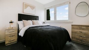 A bedroom with a bed, a nightstand, a dresser, a window with a view, and a framed picture on the wall. - Free Parking | Central | Sleeps 6 | 3 Bedrooms (North Lanarkshire)