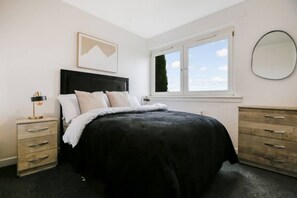 Un dormitorio con cama, mesita de noche, cómoda, ventana con vistas y un cuadro en la pared.