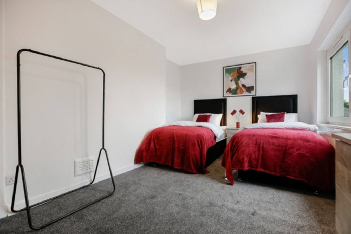 A hotel room with two beds, a standing lamp, a painting on the wall, and a window.