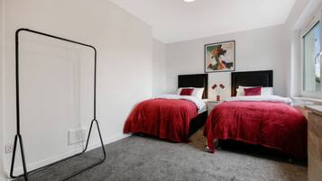 A hotel room with two beds, a standing lamp, a painting on the wall, and a window.