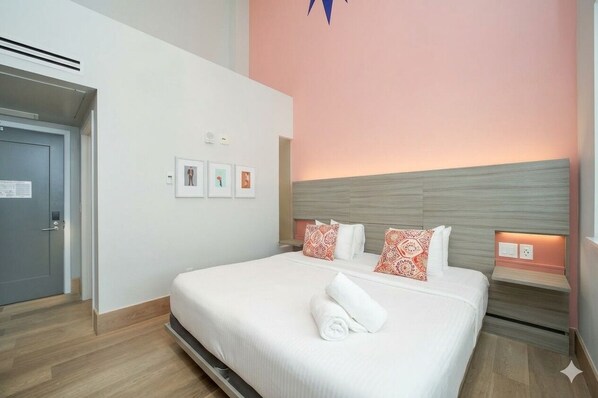Una habitación de hotel con una cama, una puerta, un respiradero instalado en la pared y una pared decorada con marcos.