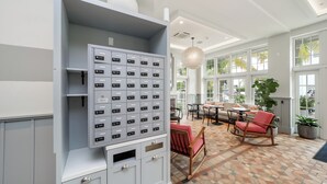 Eine Hotellobby mit einem großen Metall-Aktenschrank, einer Sitzecke mit Tisch und Stühlen sowie großen Fenstern mit Blick auf Palmen.