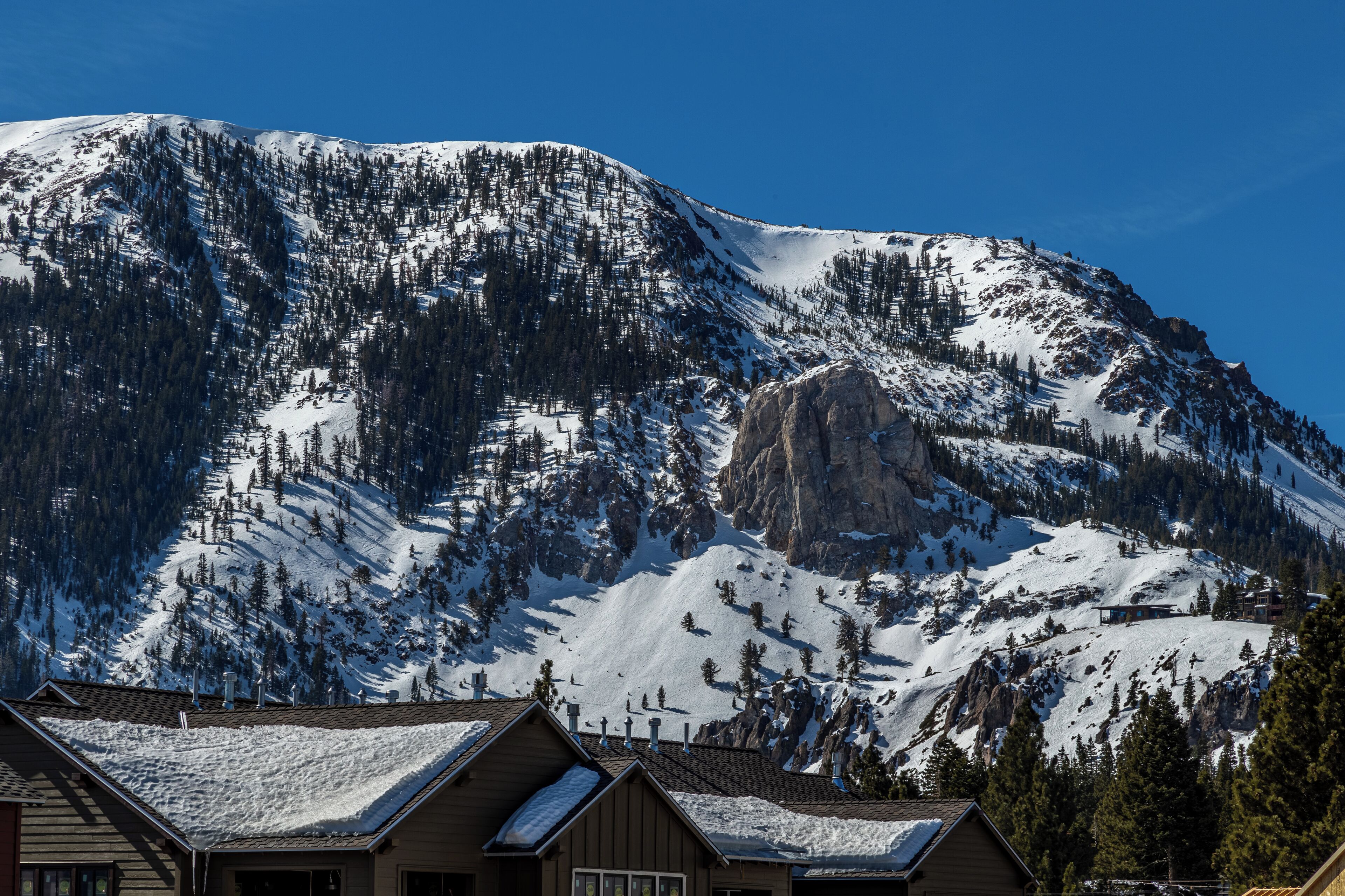 A mountain with snow-covered slopes and a cabin with a sloped roof.